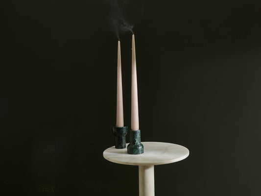 Two candles in green holders on a white pedestal against a black background