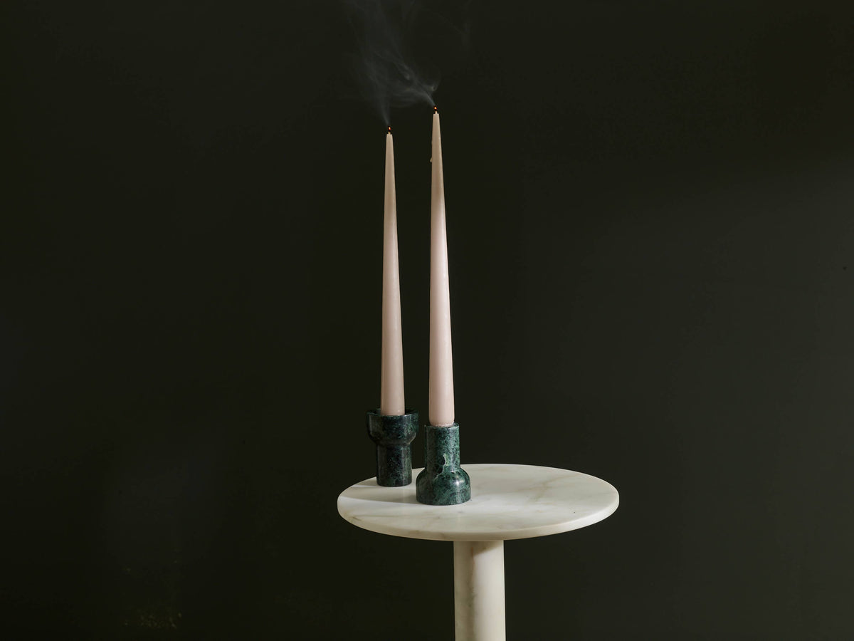 Two candles in green holders on a white pedestal against a black background