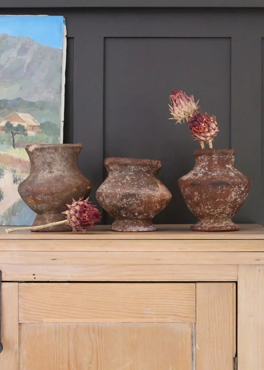 Decorative setup with rustic vases and a painting on a wooden surface against a dark wall.