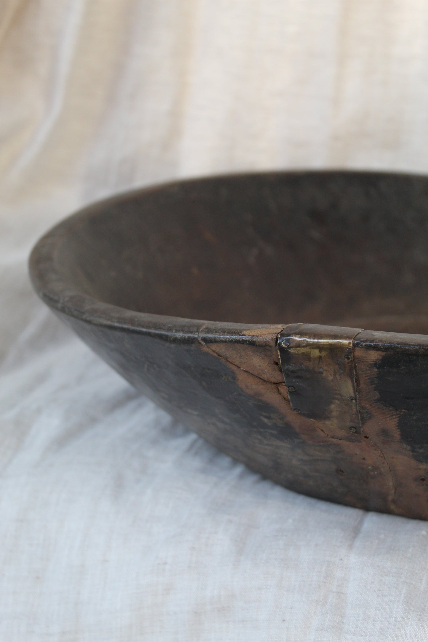 Dark wood bowl with metal fixing on beige background