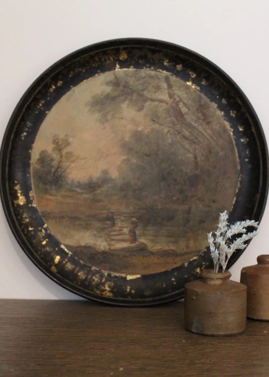 Round decorative tray with a scenic painting on a wooden surface against a white wall