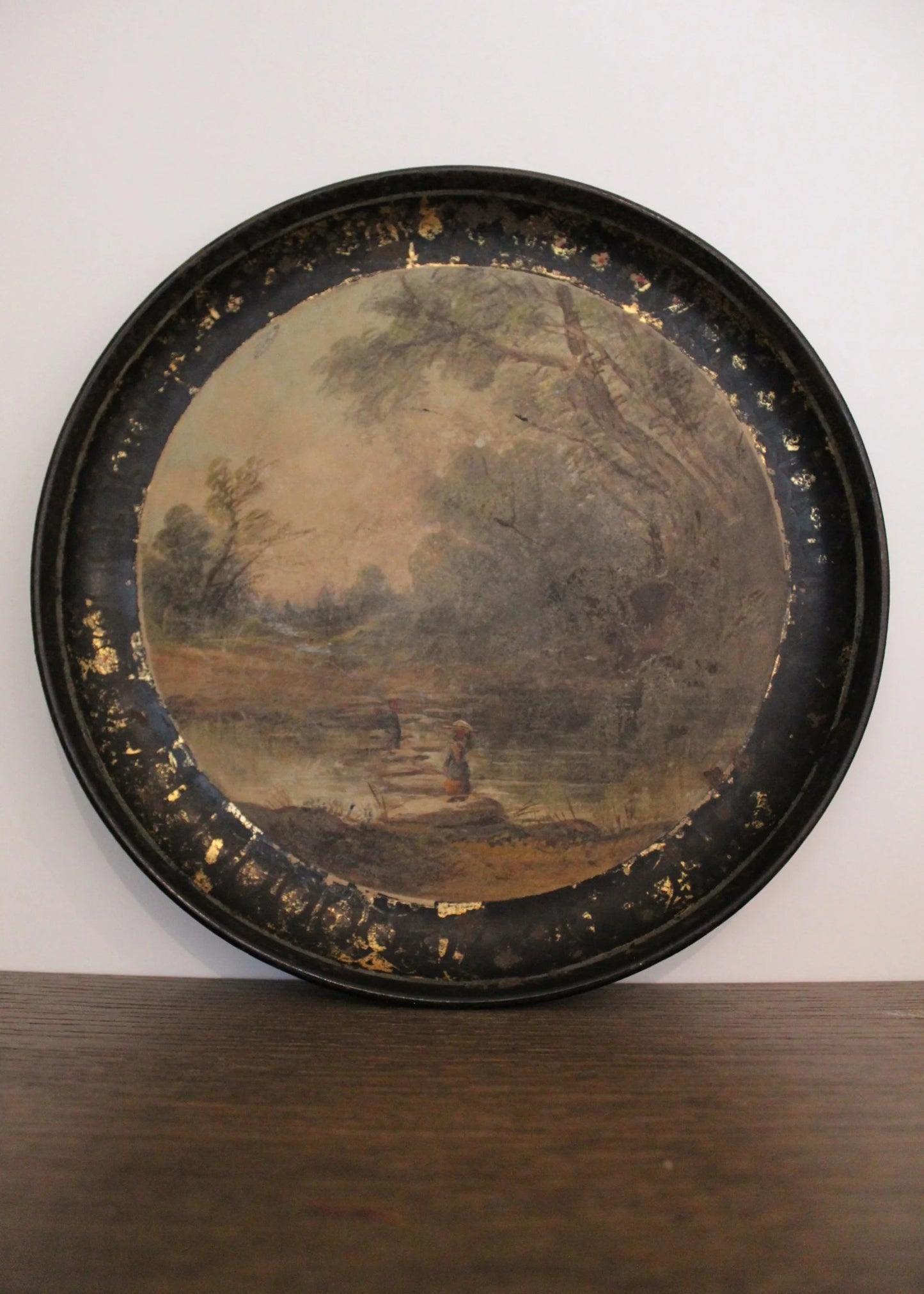 Round decorative tray with a landscape painting on a wooden surface