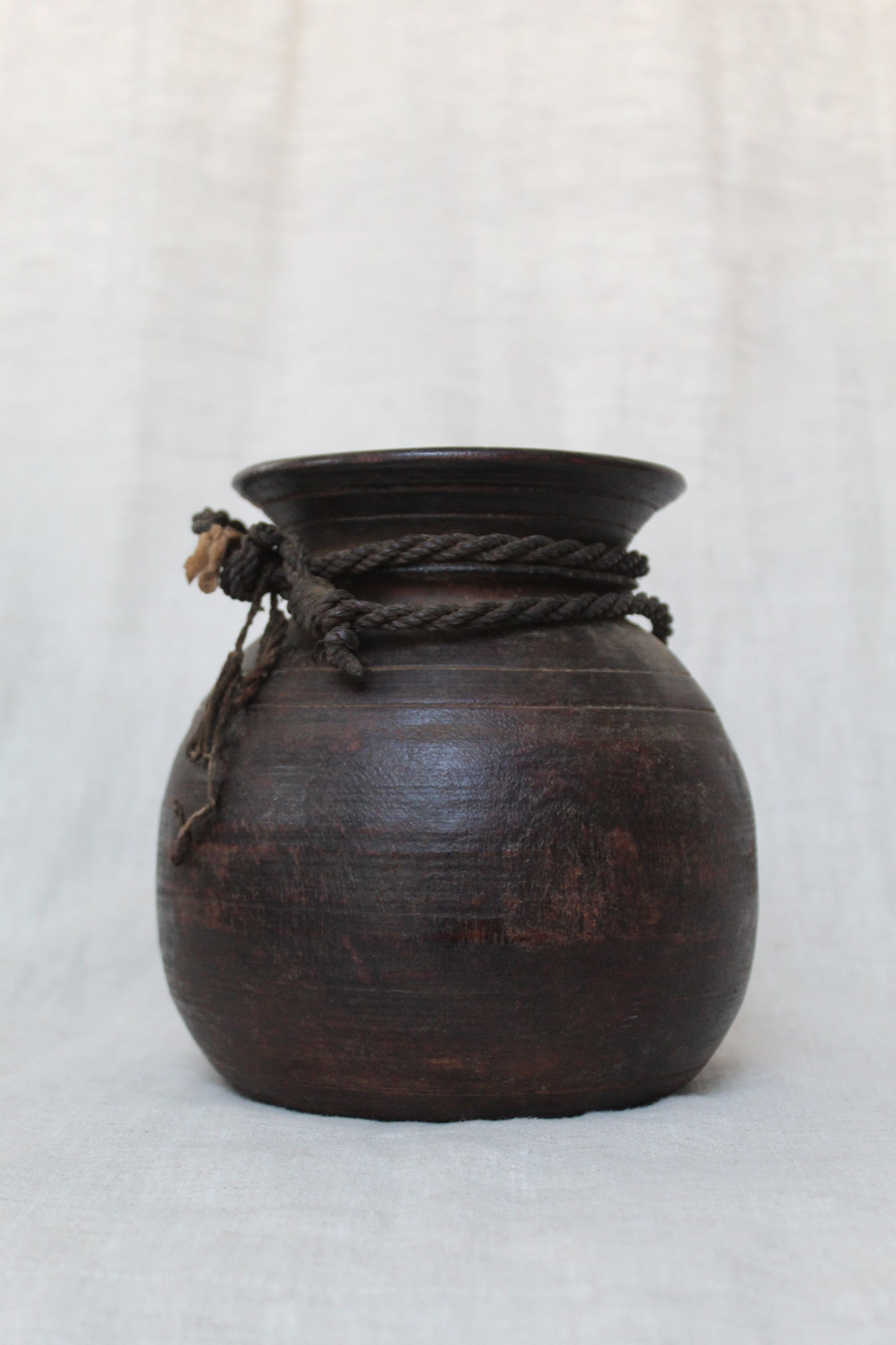 Dark wooden jar with rope handle on a light gray background