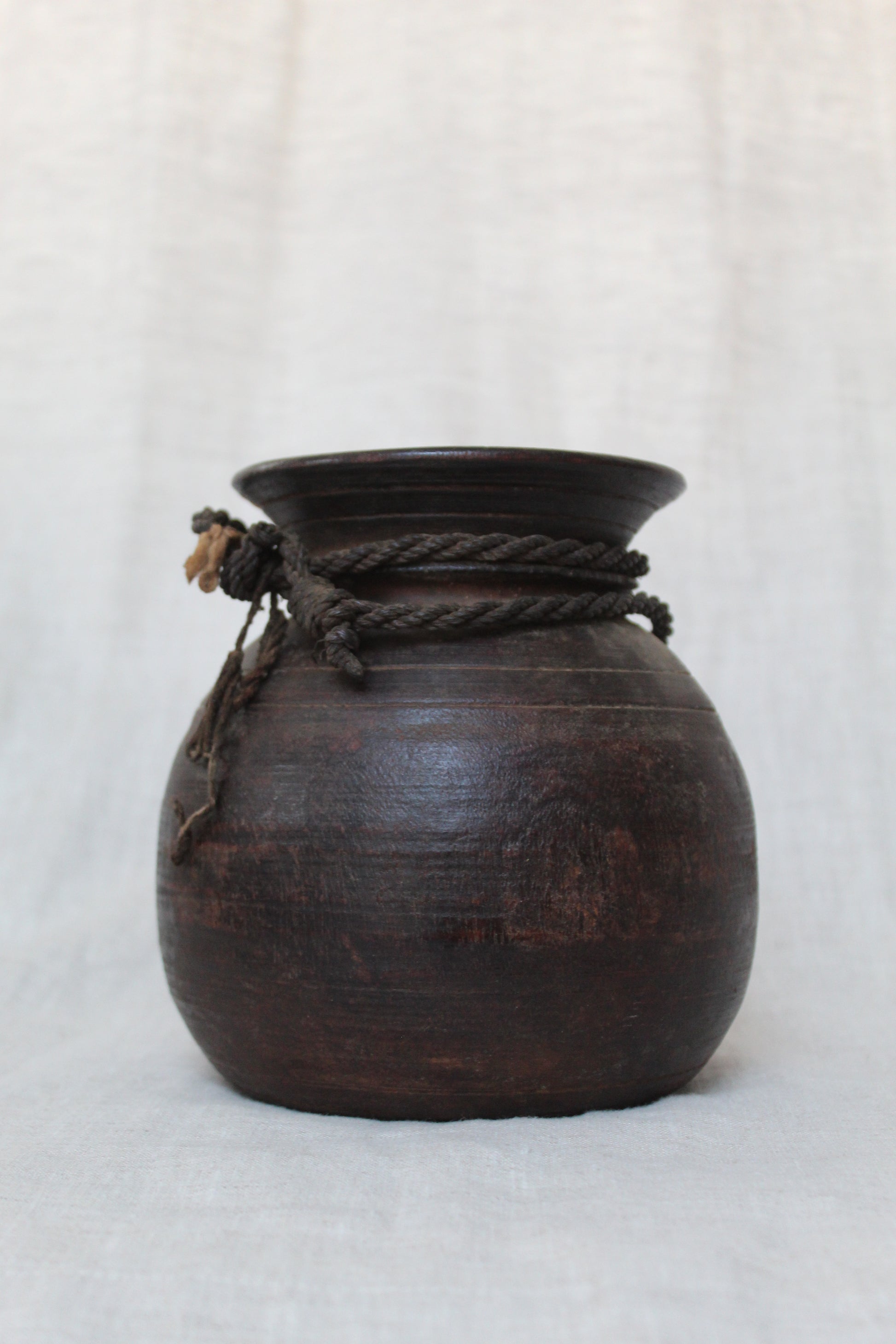 Dark wooden jar with rope handle on a light gray background