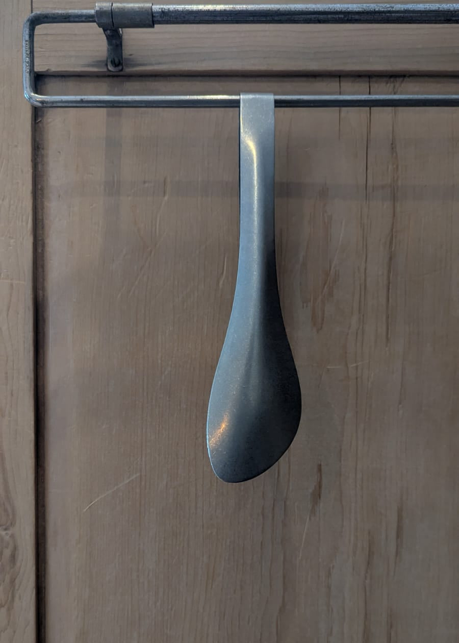 Spoon hanging on a wooden door with a metal handle.