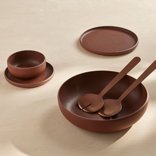 Set of brown ceramic dishes including a bowl, plate, and spoons on a beige background