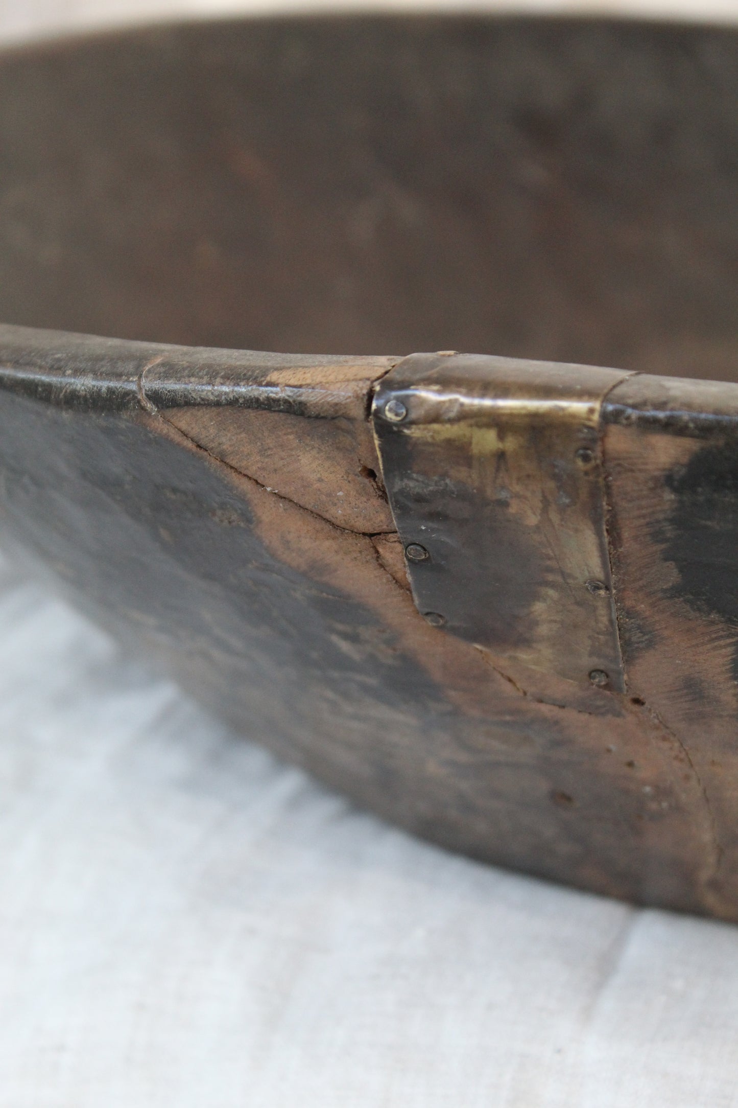 Close up of dark wood bowl with metal fixing on beige background