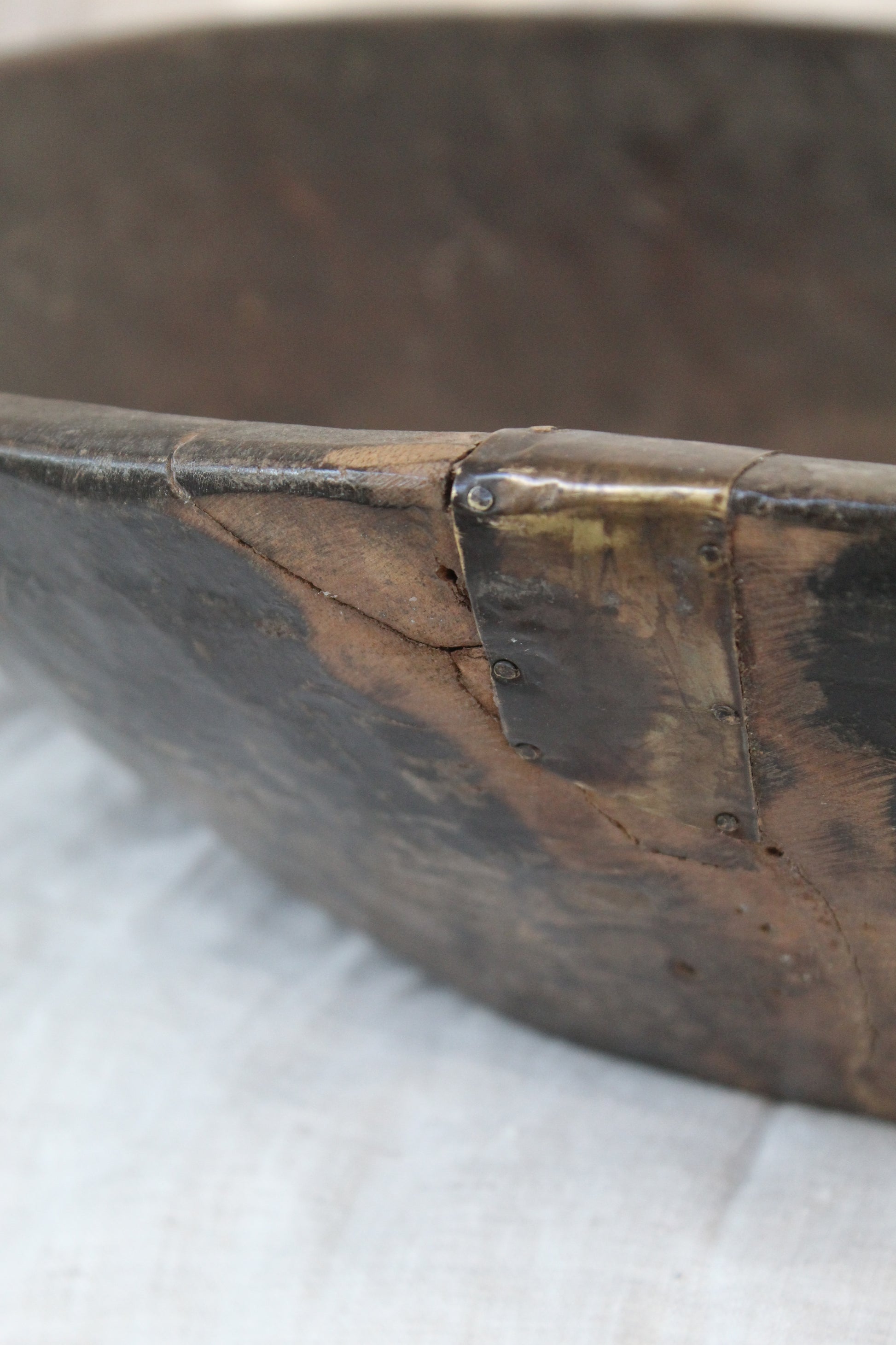 Close up of dark wood bowl with metal fixing on beige background